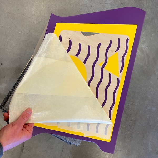 Peeling transfer tape off the yellow and purple cut vinyl graphics applied to the right side.