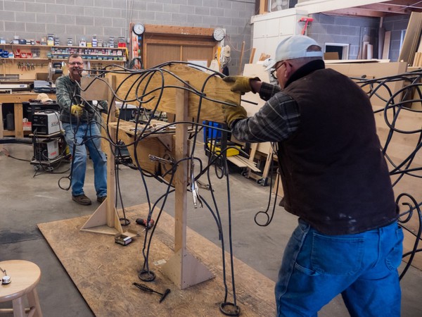 two people move a longhorn sculpture mounted to a wooden frame