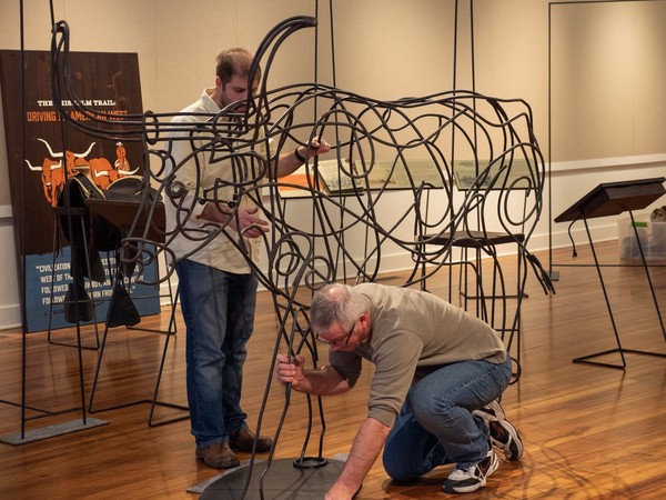 three people move longhorn sculpture into place within a gallery