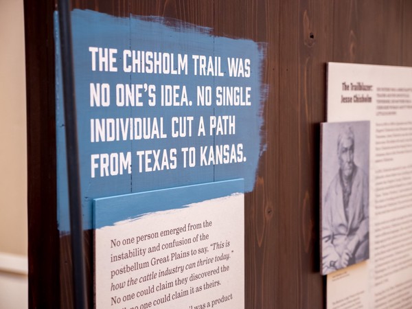 white stenciled text over blue paint with rough brush stroke edges: 'The Chisholm Trail was no one's idea. No single individual cut a path from Texas to Kansas.'