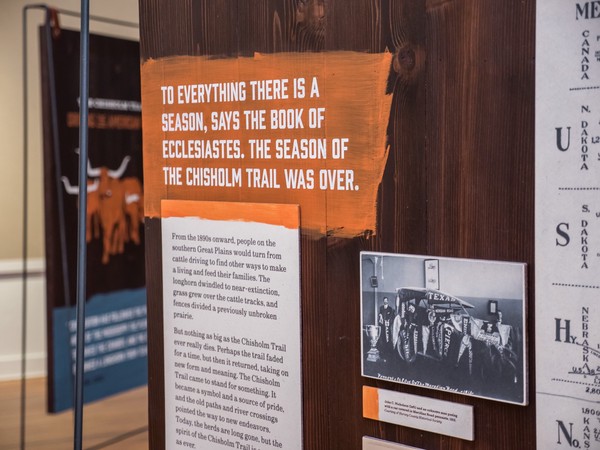 white stenciled text over roughly painted orange: 'To everything there is a season, says the Book of Ecclesiastes. The season of the Chisholm Trail was over.'