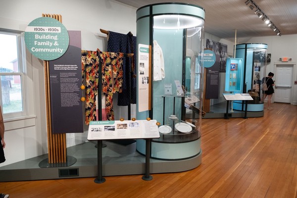 Grouping of vertical interpretive panels attached to wood slats, kimonos on stands, and a large cylindrical display case