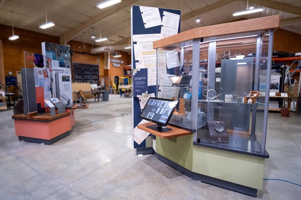 The glass sides of the display case match the trapezoid shape of the base. A maple top cap houses lights illuminating objects on glass shelves.