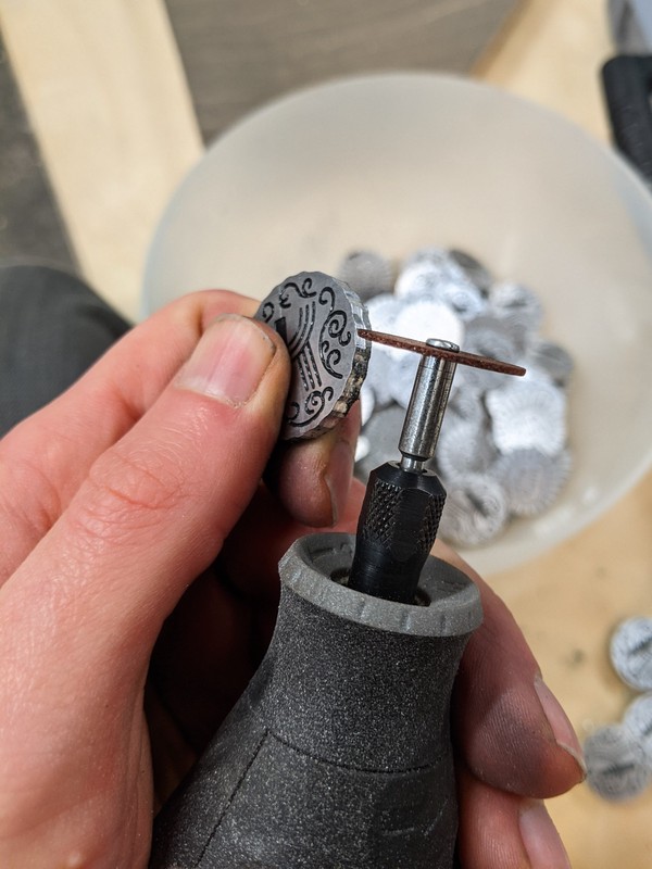 Holding the edge of a individual coin up to a rotary sanding tool to clean up the broken off tab