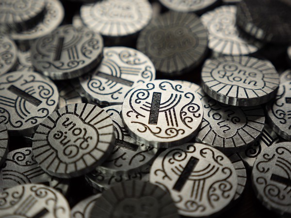 Pile of coins, focused on one featuring a stylized 'K' and curving vine patterns