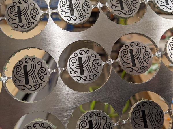 Coins suspended by narrow tabs within the circular profiles cut out of the aluminum plate