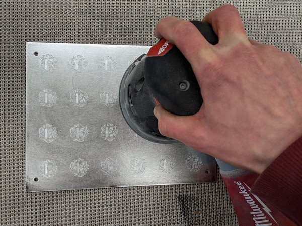 Using an orbital sander to remove the burrs raised by engraving