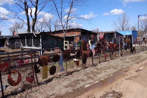 artworks made from farm implement discs and other flat metal in front of what could be decrepit chicken coops