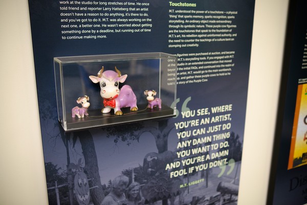 Three purple cow figurines in a case mounted on an interpretive panel