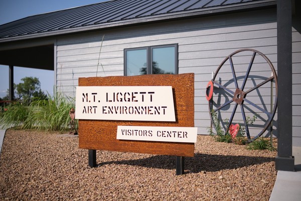 Sign made of rusted steel with white powder-coated and laser-cut panels mounted in front saying 'M.T. Liggett Art Environment Visitors Center'