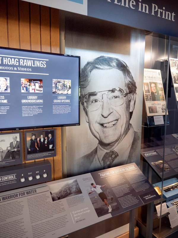 screen next to large metallic portrait of a man wearing suit-and-tie and glasses